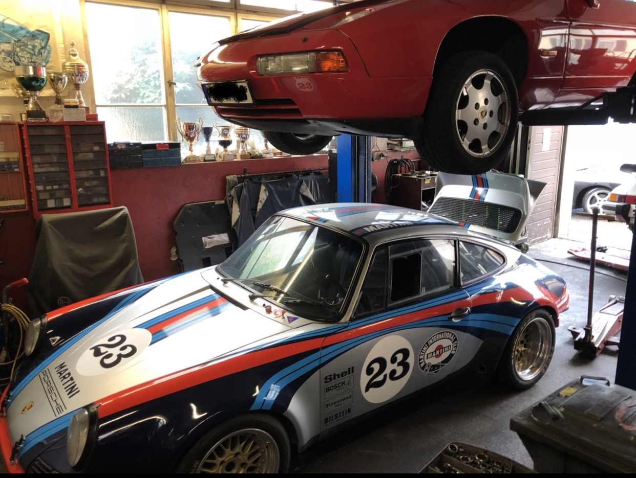 Werkstatt von Dutt Motorsport: Porsche 928 auf der Hebebühne, davor ein Porsche 911 in Martini-Rennlackierung